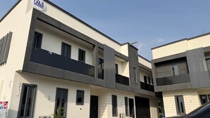 A modern two-story residential building with a flat roof, large windows, and a visible air conditioning unit. - BAE LUXURY APARTMENT (Akure)