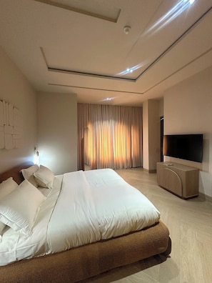 Una habitación de hotel moderna con una cama grande, un televisor de pantalla plana y un ventanal con cortinas.