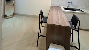 A modern kitchen with a marble countertop, a wooden dining table, two black chairs, and pendant lighting. - BAE LUXURY APARTMENT (Akure)