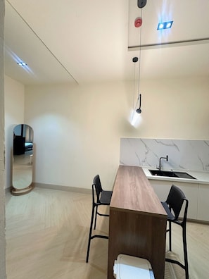 Una cocina moderna con encimera de mármol, una mesa de comedor de madera, dos sillas negras e iluminación colgante.