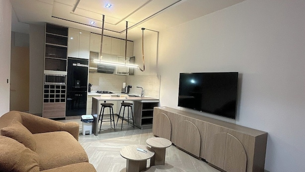 A modern living room with a sofa, a TV, a kitchen area, and a dining space. - BAE LUXURY APARTMENT (Akure)
