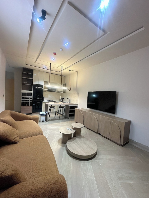 A modern living room with a sofa, a TV, a kitchen area, and a dining space. - BAE LUXURY APARTMENT (Akure)