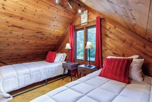 Une chambre confortable située sous les toits, avec deux lits, une table de chevet, une lampe et une fenêtre avec des rideaux.
