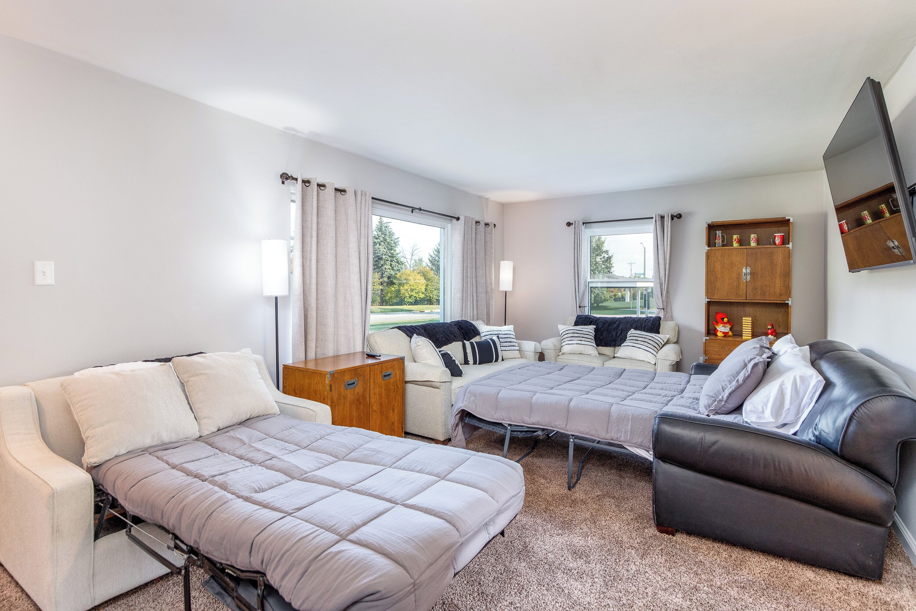 A room with two beds, a sofa, a wooden cabinet, and a TV mounted on the wall.