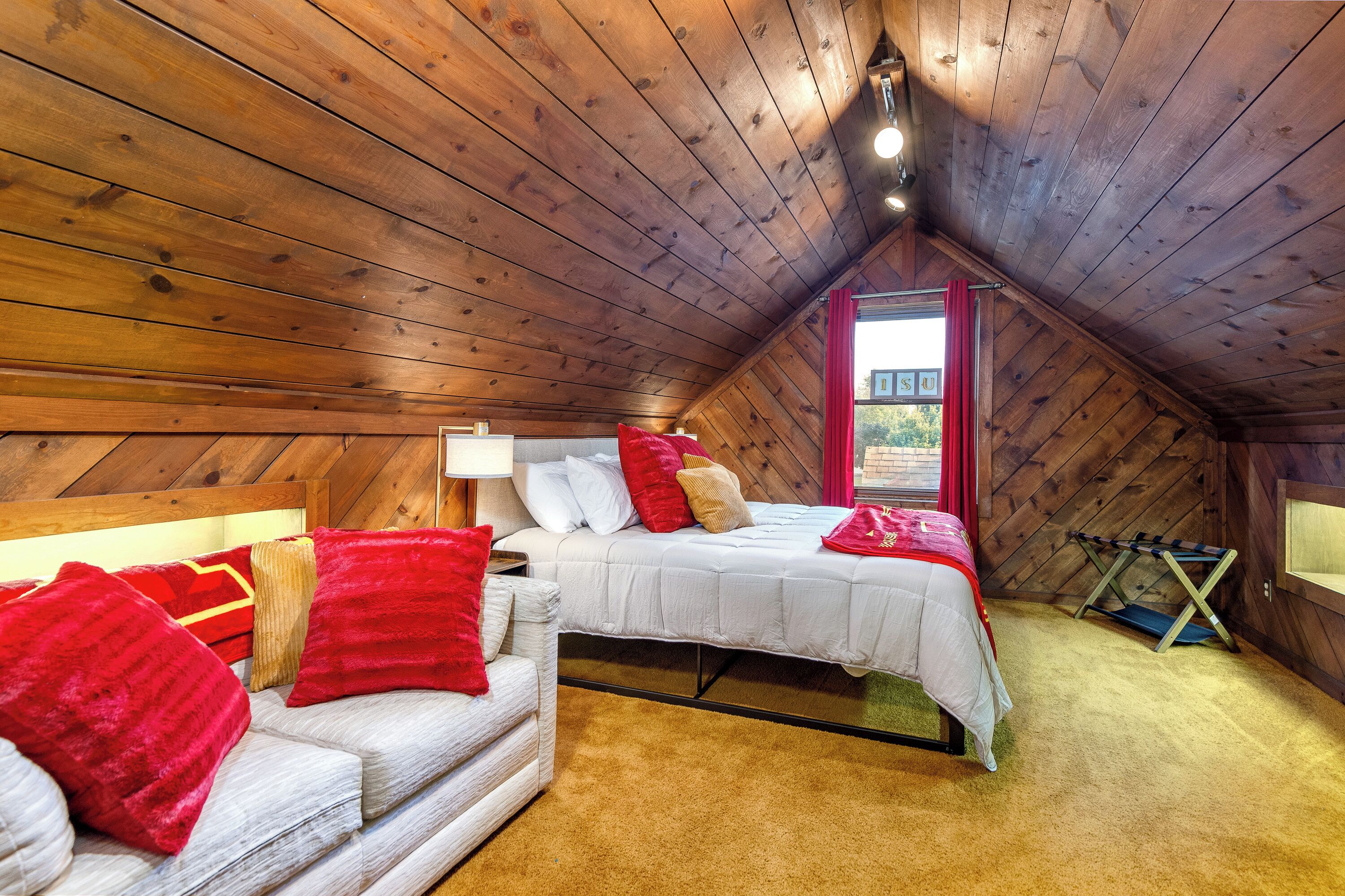 Una camera da letto mansardata accogliente, con soffitto spiovente, un letto con biancheria bianca, una tenda rossa e una piccola finestra.