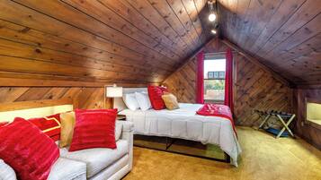 Una camera da letto mansardata accogliente, con soffitto spiovente, un letto con biancheria bianca, una tenda rossa e una piccola finestra.