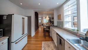 A modern kitchen with a refrigerator, stove, and sink. There is a wooden floor and a window with a view of the outside. - Charming Victorian Home | Little Italy + Garden (Toronto)