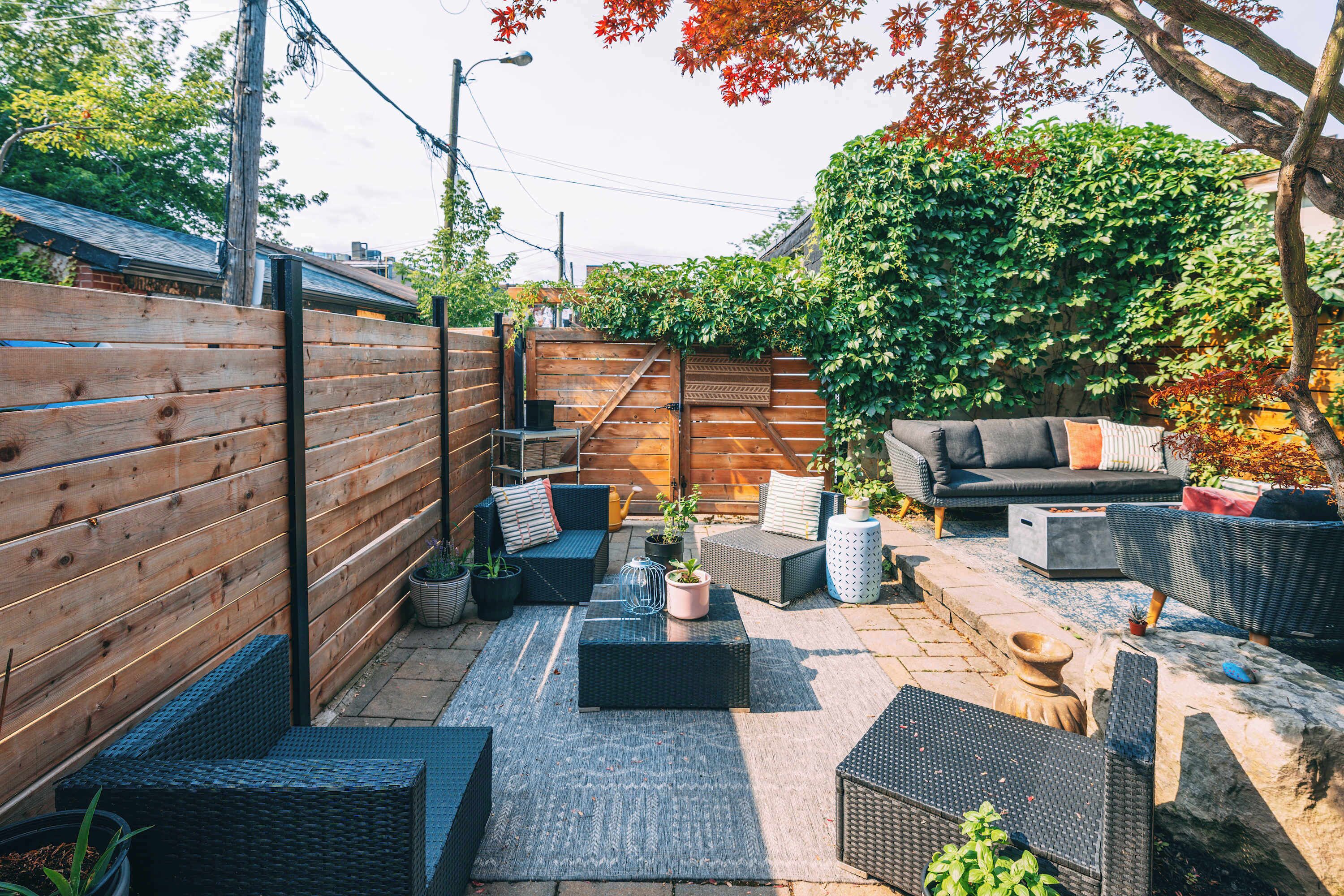 Un patio con mobiliario de mimbre, cerca de madera y diversas plantas en macetas.