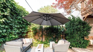 An outdoor seating area with a large umbrella, two wicker sofas, and a coffee table. - Charming Victorian Home | Little Italy + Garden (Toronto)