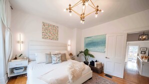 A bedroom with a large bed, bedside tables, a wall-mounted light, a ceiling light fixture, a painting, and a door. - Charming Victorian Home | Little Italy + Garden (Toronto)