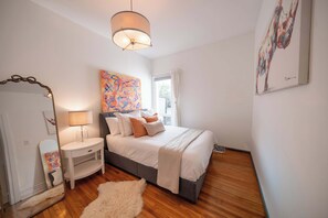 Une chambre à coucher avec un lit, une table de chevet, une lampe et un grand tableau abstrait accroché au mur.