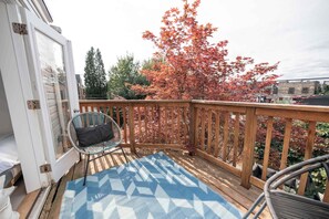 Une terrasse en bois agrémentée d’un tapis à motifs bleus, d’une chaise en osier et offrant une vue sur le feuillage automnal.
