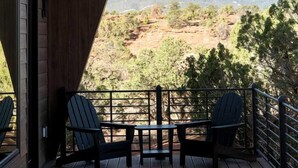 A wooden deck with two chairs and a table, overlooking a hilly landscape. - Luxury Mid-Century Retreat with Private Hot Tub Near Capitol Reef National Park, Utah (Wayne County)