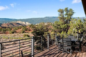 Eine Holzterrasse mit Tisch und Stühlen, die auf eine gebirgige Landschaft mit spärlicher Vegetation blickt.
