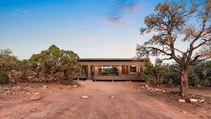 A modern two-story building with a dirt driveway and surrounding natural landscape. - Luxury Mid-Century Retreat with Private Hot Tub Near Capitol Reef National Park, Utah (Wayne County)