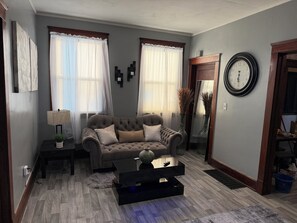 A living room with a sofa, a coffee table, and a clock on the wall. - SMOKE FRIENDLY Lovely 1-bedroom apartment with AC in vibrant Racine (Racine)