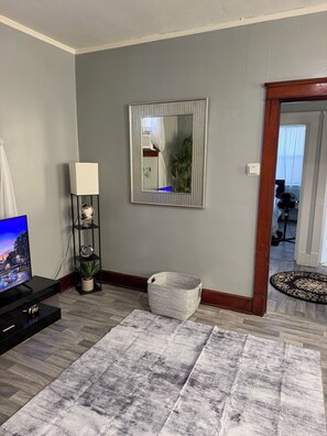 A living room with a flat-screen TV, a white lamp, a mirror, a woven basket, and a patterned rug. - SMOKE FRIENDLY Lovely 1-bedroom apartment with AC in vibrant Racine (Racine)
