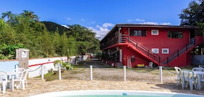 A red building with a pool area, surrounded by greenery and a clear sky. - Suite Quadrupla a 400m da Praia de Itamambuca (Ubatuba)