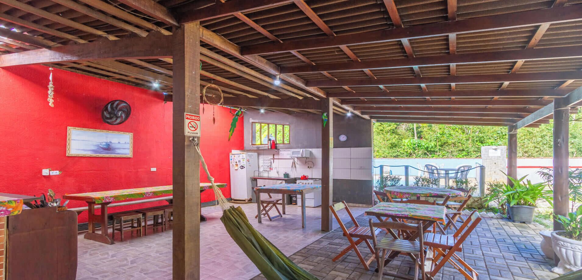 A covered outdoor area with tables and chairs, a red wall, and a kitchen area.