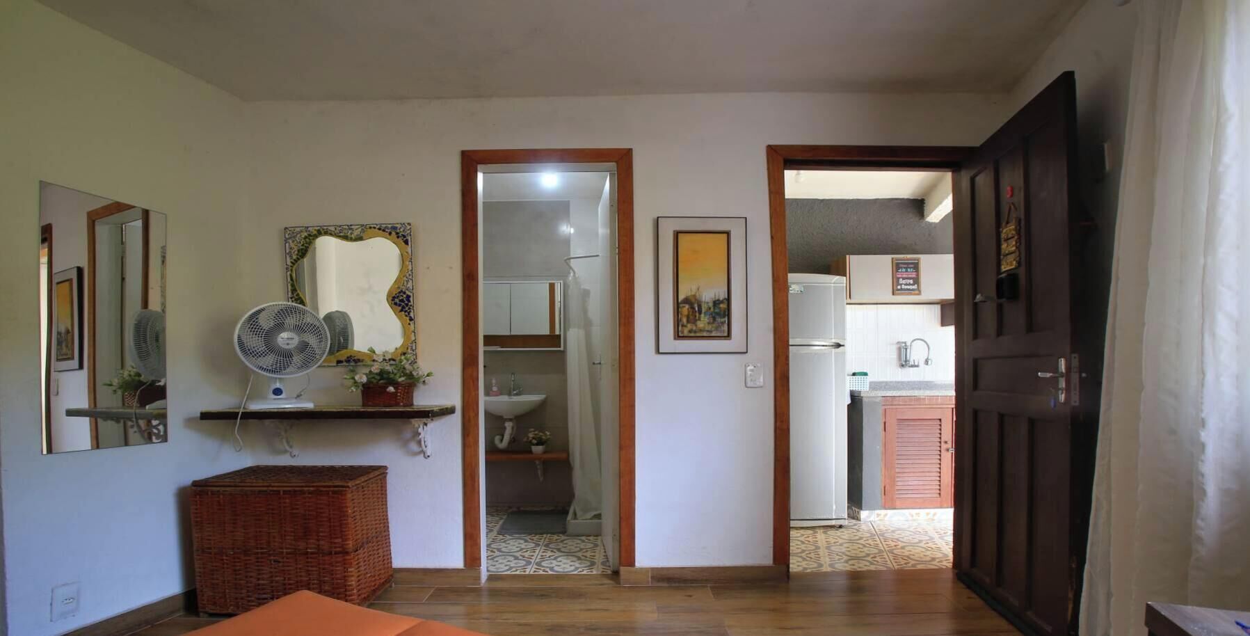A hallway leading to a bathroom and kitchen area with a fan, mirror, and a framed picture on the wall.