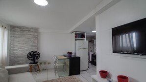 Un menjador modern amb televisió de pantalla plana, zona de dinar amb taula de vidre i cuina amb nevera.