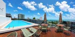 Uma área de piscina no terraço com vista para o oceano, cercada por espreguiçadeiras e guarda-sóis.