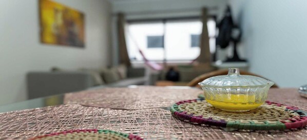 Uma mesa com um jogo americano tecido e uma tigela de vidro contendo um líquido amarelo, possivelmente óleo, sobre um apoio de mesa tecido.