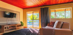 A living room with a television, a sofa, a coffee table, and a sliding glass door leading to a balcony. - Sitio em Campinas com Piscina e Churrasqueira (Campinas)
