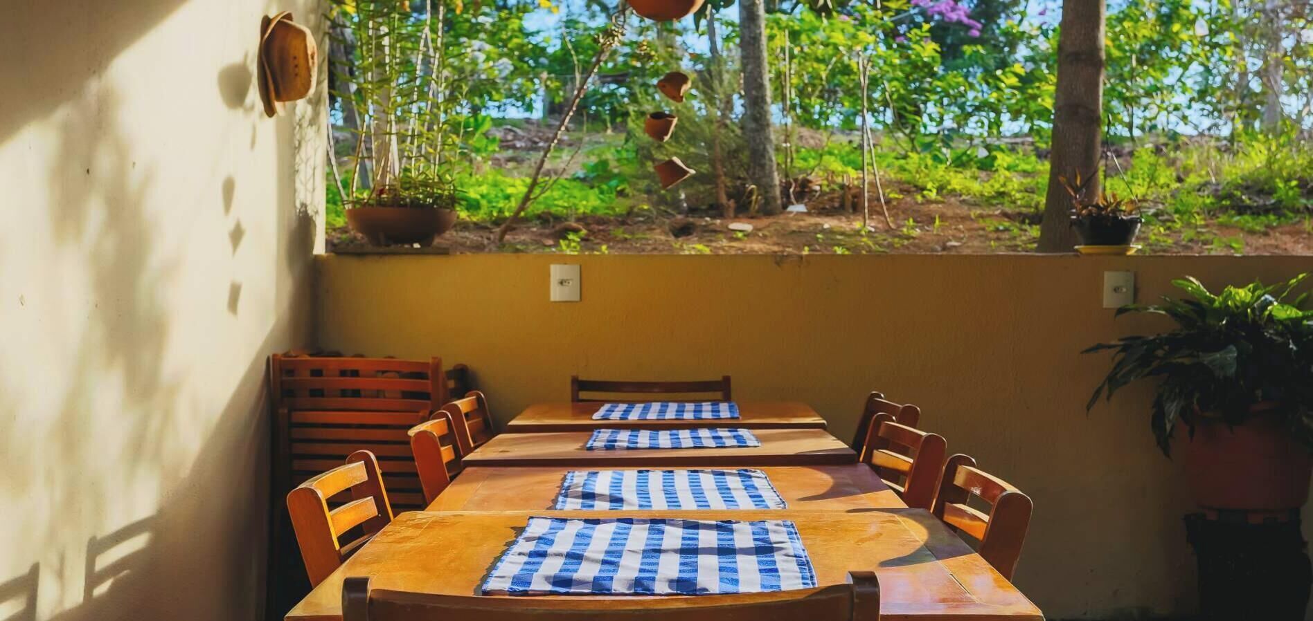 An outdoor dining area with wooden tables and chairs, blue and white checkered tablecloths, and potted plants.