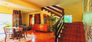 A spacious living area with a wooden staircase, a dining table with chairs, a cabinet, and a potted plant. - Sitio em Campinas com Piscina e Churrasqueira (Campinas)