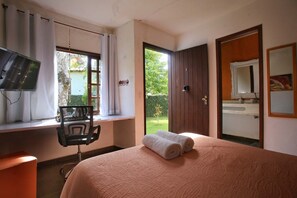 Ein Schlafzimmer mit einem Bett, einem Schreibtisch mit Stuhl, einem Fernseher und einer Tür, die auf einen Balkon führt.