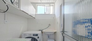 Een kleine badkamer met een wasmachine, een wastafel en een raam.