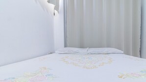 Huone, jossa on sänky, ikkuna, jossa on verhot, ja seinään kiinnitetty valaisin.