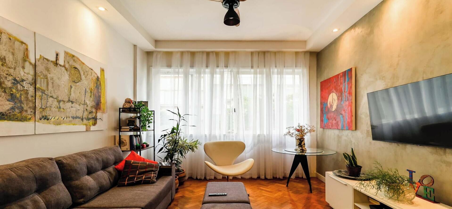 A living room with a sofa, a chair, a TV, and a small table with plants.