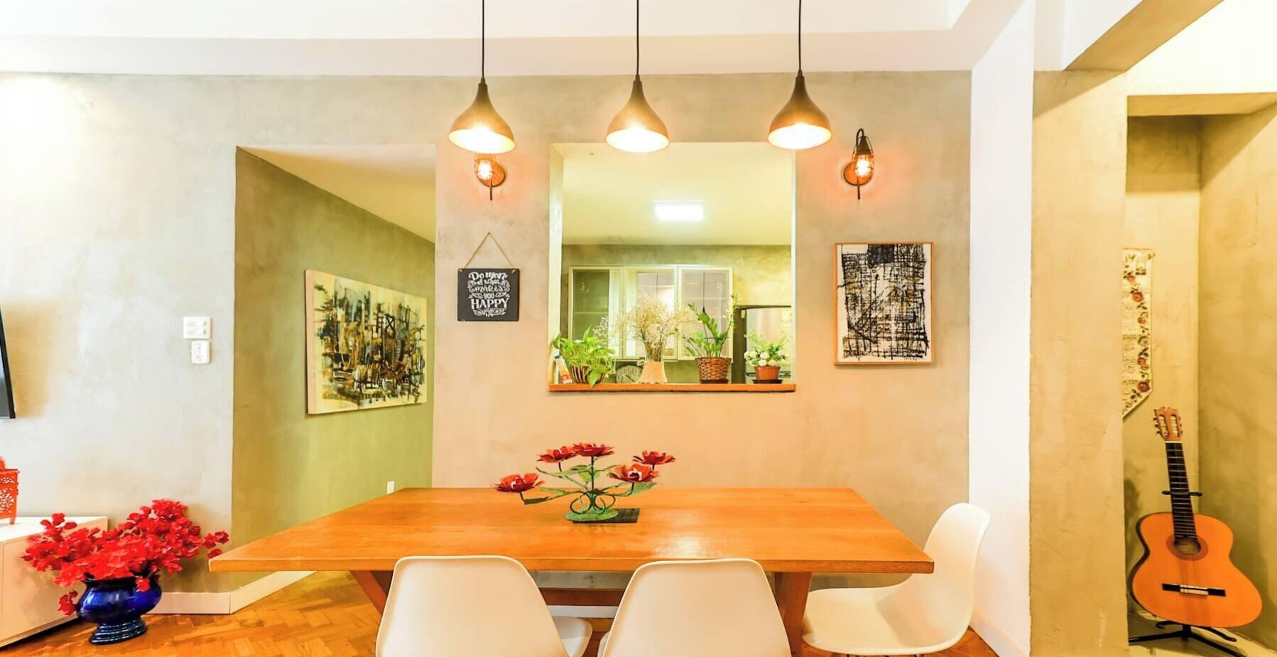 A dining area with a wooden table, white chairs, hanging pendant lights, and a guitar leaning against the wall.