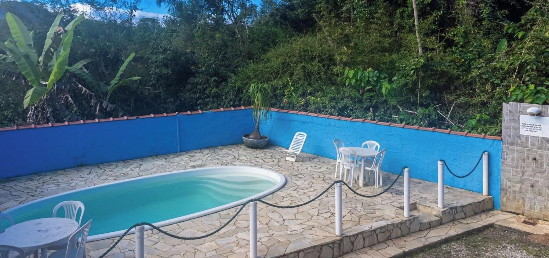 Ein Außenpool mit Steinböden, umgeben von einer blauen Wand und weißen Stühlen.