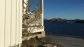 A coastal building with a balcony overlooking a body of water and distant mountains. - Apartment with sea view in Henningsvær (Vågan)