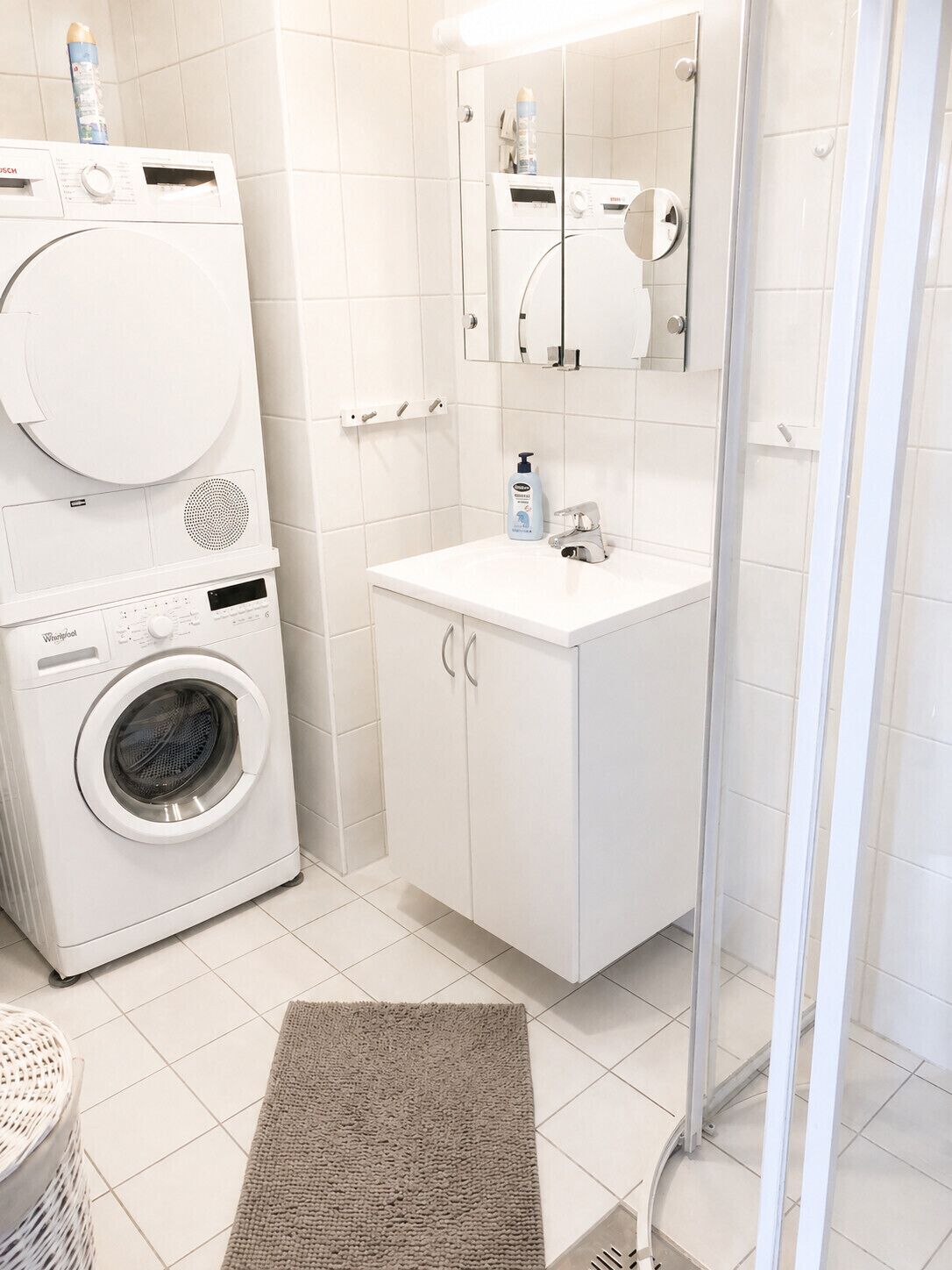 Un baño moderno con lavadora y secadora apiladas, un lavamanos con espejo y cabina de ducha.