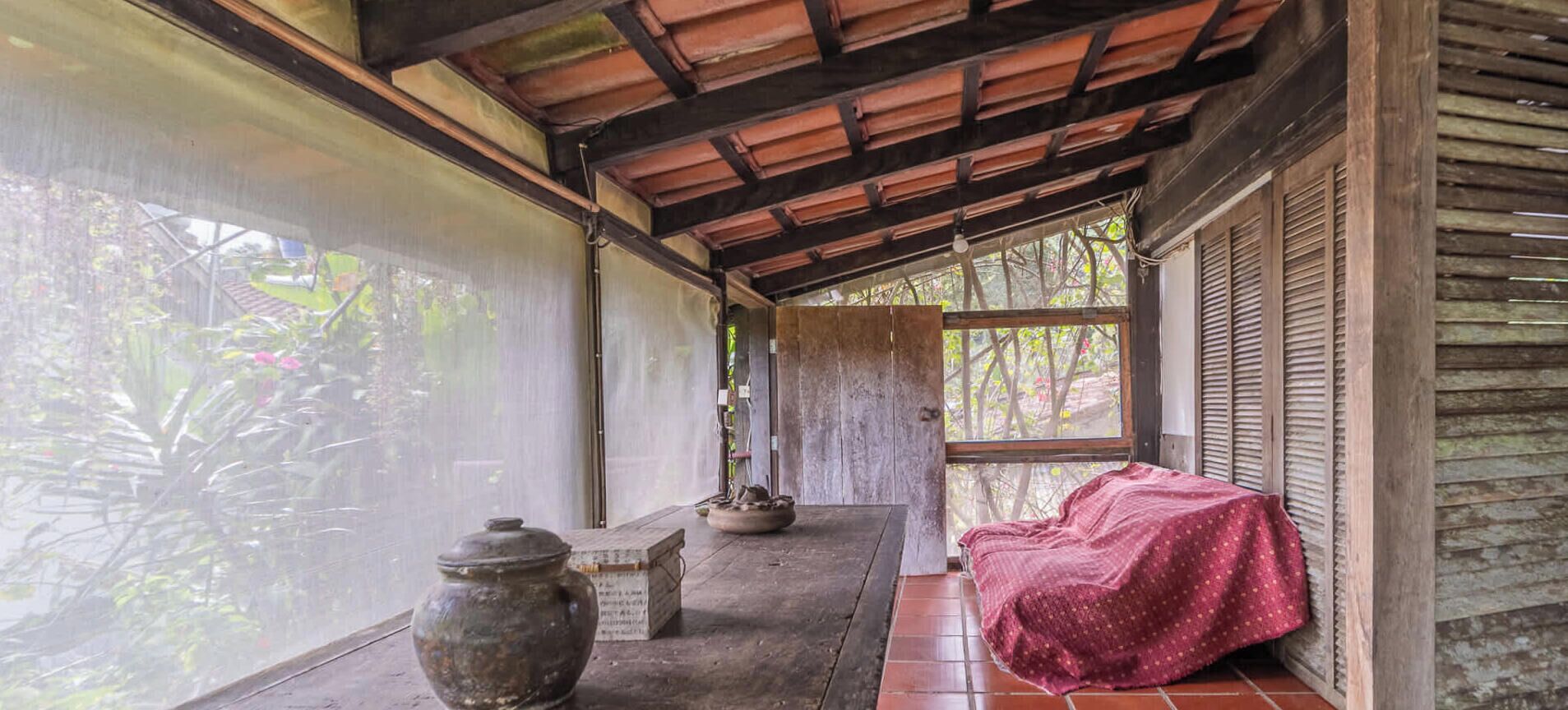 A covered porch with a bench, a table, and a large pot.