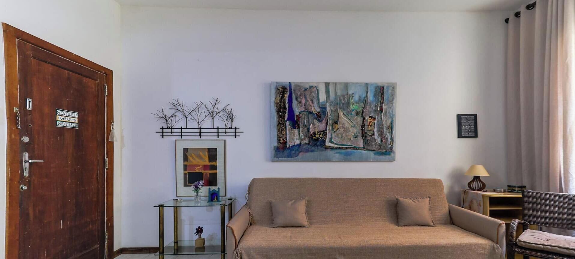 A room with a beige sofa, a glass coffee table with a vase, a painting on the wall, and a wooden door.