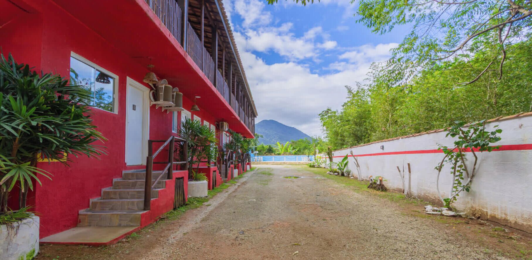 Un bâtiment rouge avec un escalier menant à l’entrée, entouré de verdure et sous un ciel dégagé.