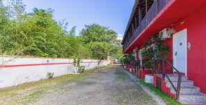 A pathway leading to a building with a red facade, a white wall with a red stripe, and a staircase with a red railing. - Suite em Ubatuba a 400m da Praia de Itamambuca (Ubatuba)