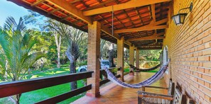 A covered outdoor area with a hammock, brick walls, and a view of a green landscape. - Sitio em Atibaia com piscina e churrasqueira (Atibaia)