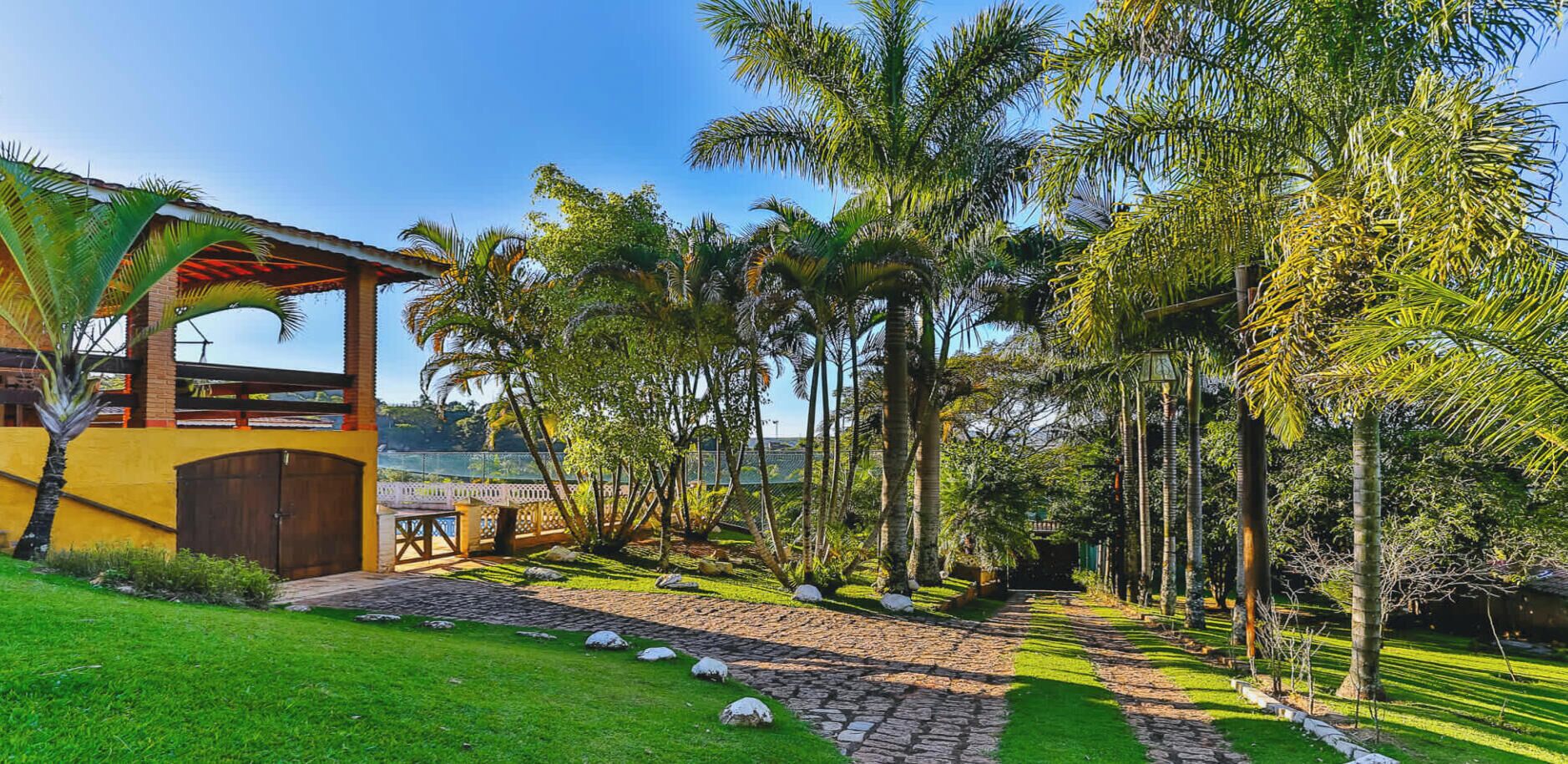 A well-maintained garden with a paved walkway, palm trees, and a building with a covered patio area.
