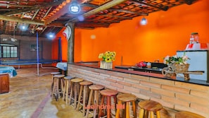 A bar area with wooden stools, a brick counter, and a wall with a bright orange color. - Sitio em Atibaia com piscina e churrasqueira (Atibaia)