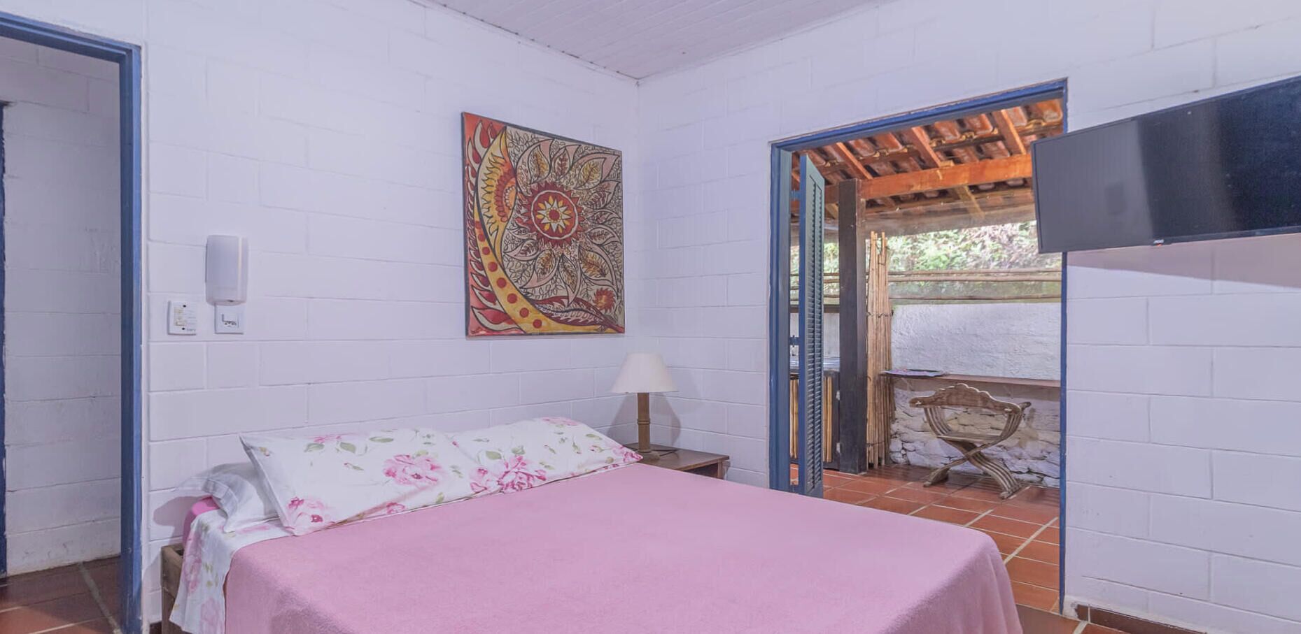 Ein Schlafzimmer mit einem Bett, einem Wand-Fernseher, einem Wandbild und einem Fenster mit Blick nach draußen.