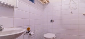 A bathroom with white tiles, a sink, toilet, and a shower area. - Residence Picinguaba: Suite a 50m da praia (Ubatuba)