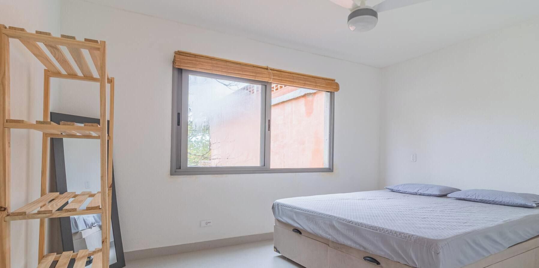 A bedroom with a bed, a window with a blind, and a wooden shelf unit.