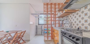 A kitchen with a gas stove, a wooden dining table with chairs, and a decorative partition. - Casa em Sao Sebastiao Frente a Praia com Vista (sao sebastiao)