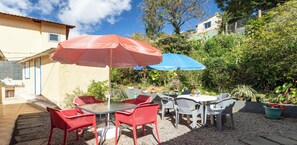 An outdoor patio with a table and chairs, two umbrellas, and potted plants. - Casa Charmosa em Miguel Pereira com Churrasqueira (Miguel Pereira)